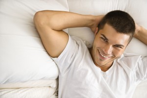 High angle view of handsome Caucasian mid adult man lying with hands behind head smiling.